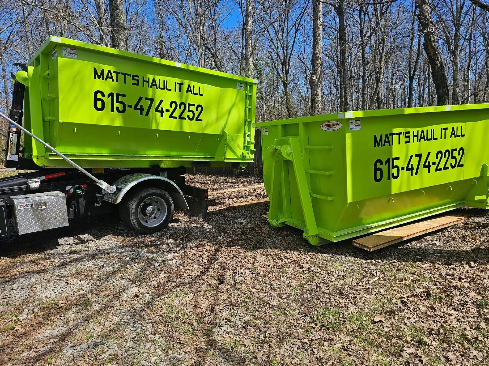Two lime green roll-off dumpsters on a wooded lot
